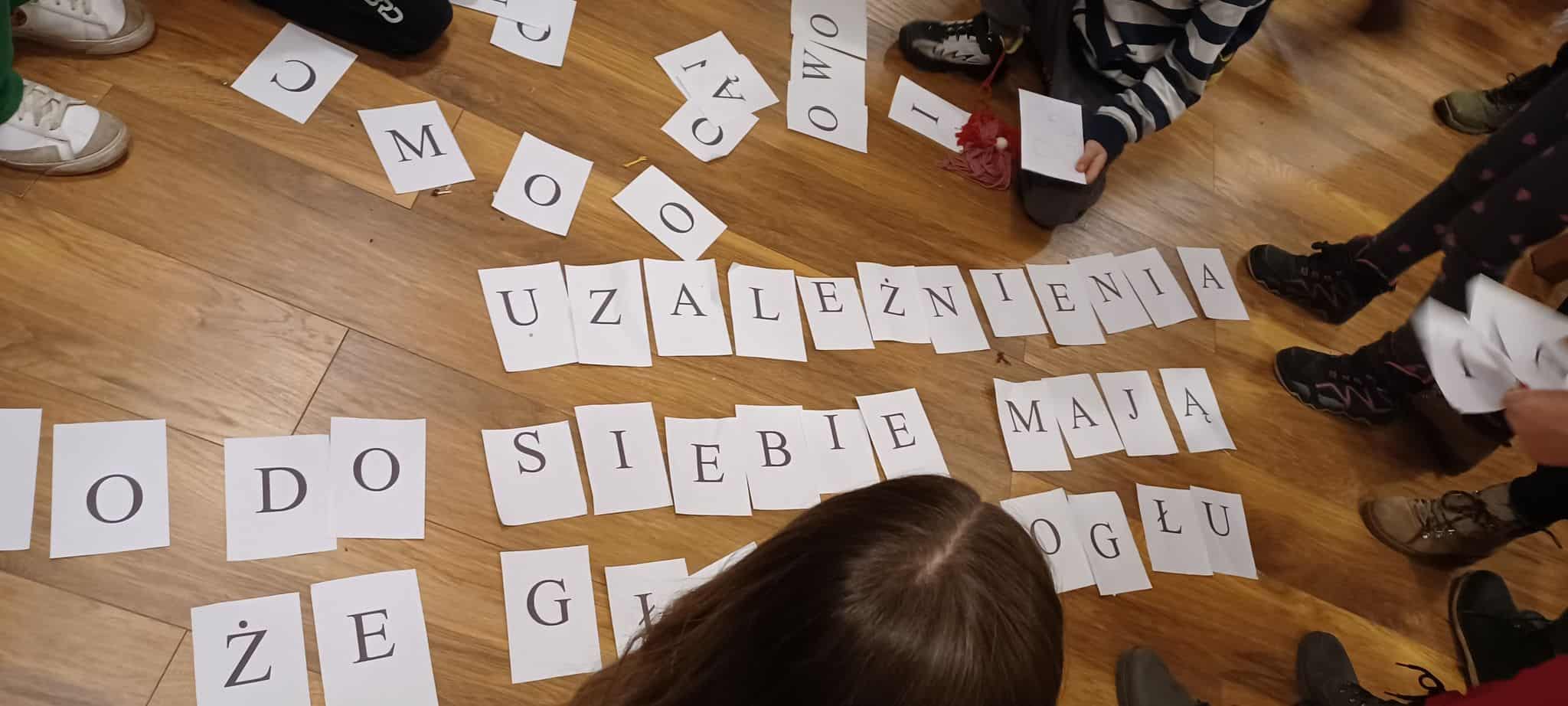 kartki z literami drukowanymi rozsypane po podłodze, dzieci układają z nich hasło