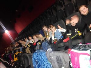 wysjcie do kina, grupa dzieci siedzi w jednym rzędzie w sali kinowej, inne rzędy puste, ściany sali ciemne