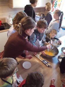 grupa dzieci stoi przy kuchennym blacie, mieszają składniki ciasta w miskach