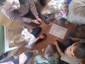 widok z góry; dzieci skupione w kręgu wokół kartki na której narysowane są twarze z emocjami
