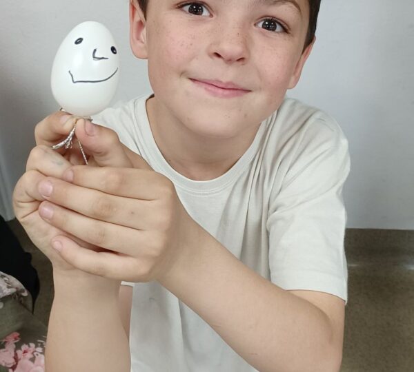 chłopiec w miałej koszulce prezentuje białe jajko z narysowaną minką