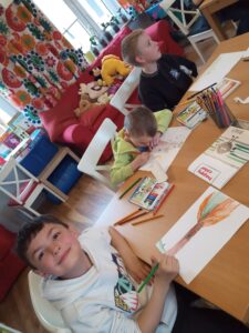 Dzieci siedzą przy stole i rysuje kredkami obrazki.
