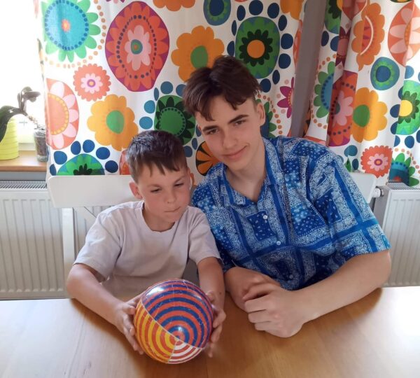dwóch chłopców siedzi przy stole, młodszy trzyma przezd soba kolorowa piłkę