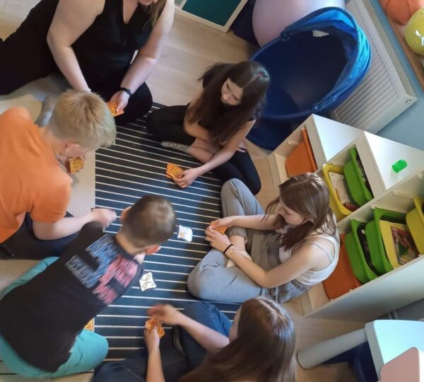 sześć osób siedzi na dywanie i gra w grę planszową