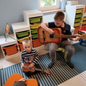 dwóch chłopców siedzi w kolorowym pokoju, grają na gitarach