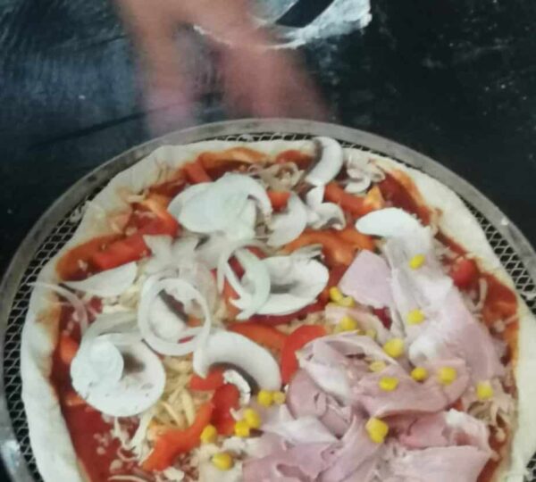 pizza przed upieczeniem, na cieście leżą kawałki pieczarek, szynki, cebuli, papryki