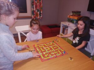Trzy dziewczynki graja w grę planszową rozłożoną na stole