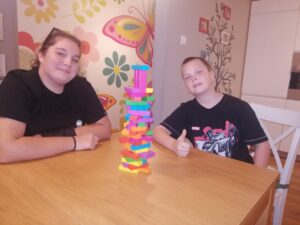 dwoje dzieci przy stole, przed nimi wieża Jenga ułożona z kolorowych klocków