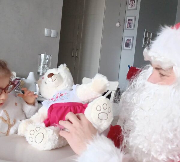 zdjęcie przedstawia małą dziewczynkę w okularach, której Mikołaj wręcza misia maskotkę.