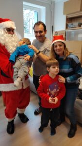 Mikołaj trzyma na rękach dziecko, obok stoi tata, pani psycholog z hospicjum oraz chłopczyk w czerwonej bluzie.