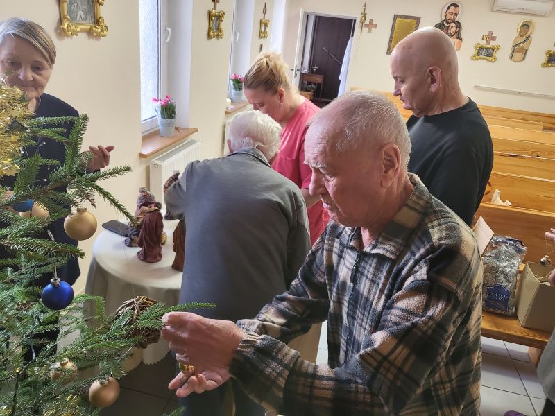 seniorzy wraz z opiekunką ubieraja choinkę, w tle wystrój kaplicy hospicyjnej